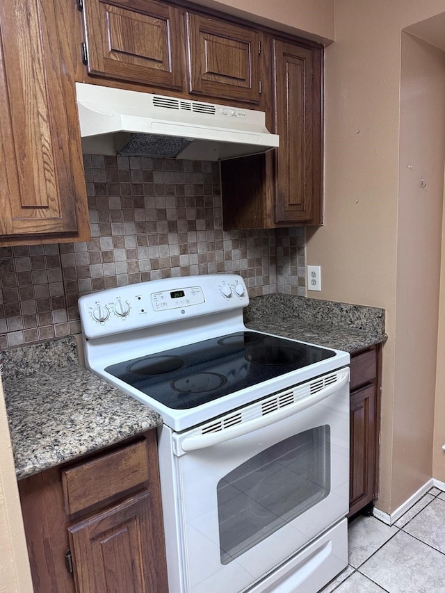 kitchen featuring light tile patterned flooring, dark stone counters, tasteful backsplash, and white range with electric stovetop