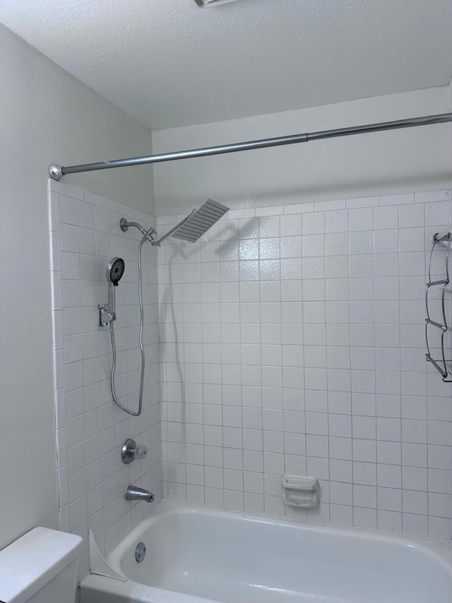 bathroom featuring toilet, tiled shower / bath, and a textured ceiling