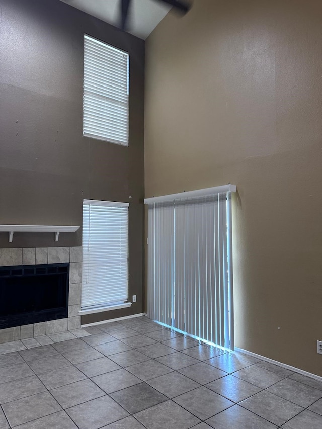 unfurnished living room featuring a tiled fireplace, light tile patterned floors, and a high ceiling