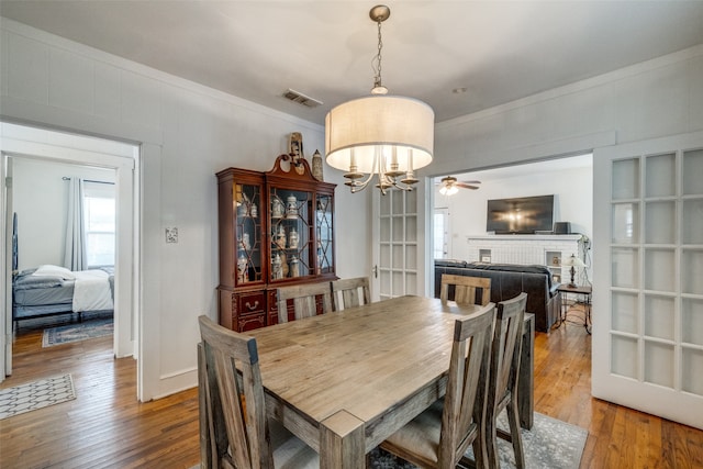 dining area with wood-type flooring, ceiling fan with notable chandelier, a fireplace, and crown molding