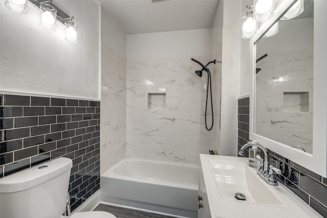 full bathroom with tile walls, tiled shower / bath combo, vanity, and toilet