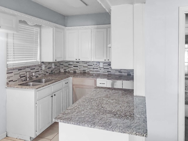 kitchen with sink, kitchen peninsula, backsplash, light tile patterned floors, and white cabinetry