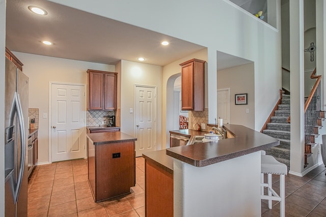 kitchen with a breakfast bar, kitchen peninsula, decorative backsplash, a kitchen island, and stainless steel fridge with ice dispenser