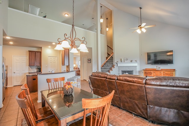 tiled dining area featuring a fireplace, high vaulted ceiling, and ceiling fan with notable chandelier