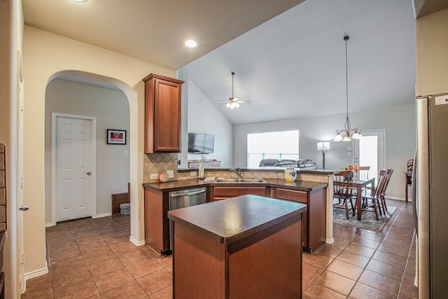 kitchen featuring tasteful backsplash, ceiling fan with notable chandelier, a kitchen island, sink, and stainless steel refrigerator