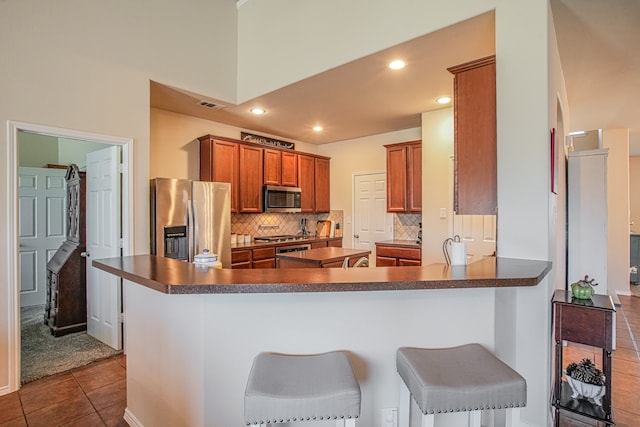 kitchen with kitchen peninsula, appliances with stainless steel finishes, dark tile patterned flooring, and a breakfast bar area