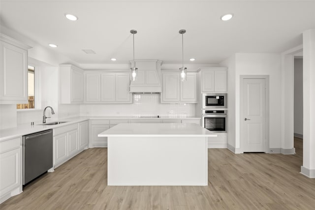 kitchen featuring a kitchen island, sink, pendant lighting, light wood-type flooring, and appliances with stainless steel finishes