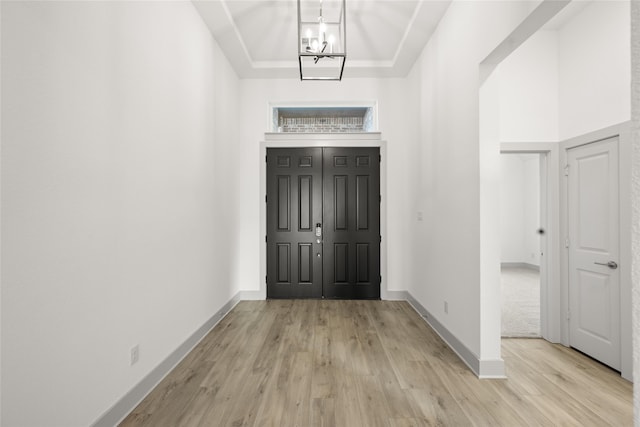 entryway with a notable chandelier, light hardwood / wood-style floors, and a raised ceiling