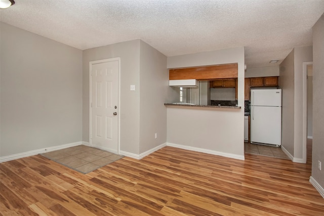 kitchen with white refrigerator, light wood-type flooring, kitchen peninsula, and a textured ceiling