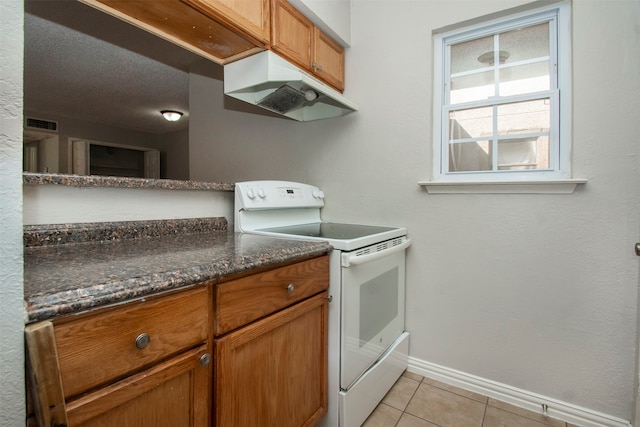 kitchen with dark stone countertops, white range with electric cooktop, light tile patterned floors, and a textured ceiling