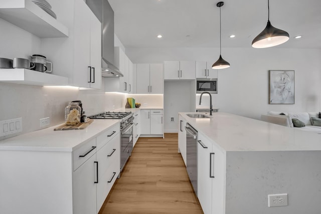 kitchen featuring stainless steel appliances, light wood-style floors, white cabinets, a sink, and wall chimney range hood