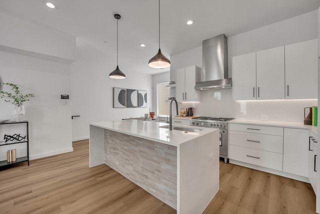 kitchen with wall chimney exhaust hood, stainless steel range, light countertops, and a sink