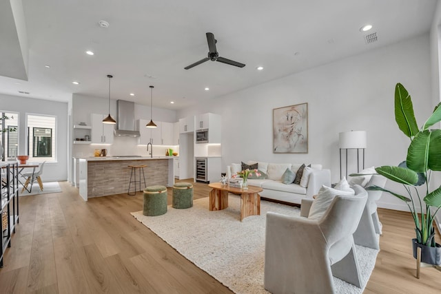 living area with ceiling fan, beverage cooler, light wood-type flooring, and recessed lighting