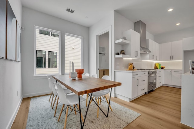 kitchen with white cabinets, wall chimney exhaust hood, light wood-type flooring, and high end range