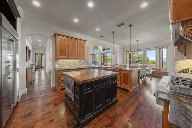 kitchen with pendant lighting, a kitchen island, dark hardwood / wood-style flooring, and built in appliances