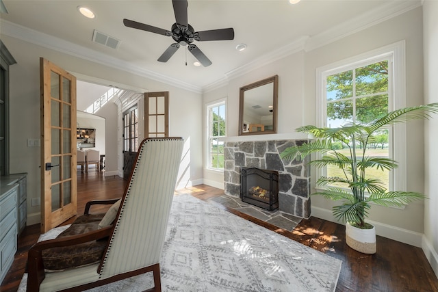 living area with ceiling fan, french doors, a stone fireplace, dark hardwood / wood-style floors, and ornamental molding