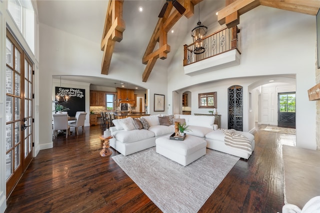 living room with beam ceiling, dark wood-type flooring, high vaulted ceiling, and a chandelier