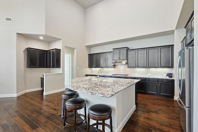 kitchen with stainless steel appliances, light stone countertops, dark hardwood / wood-style floors, and a center island with sink