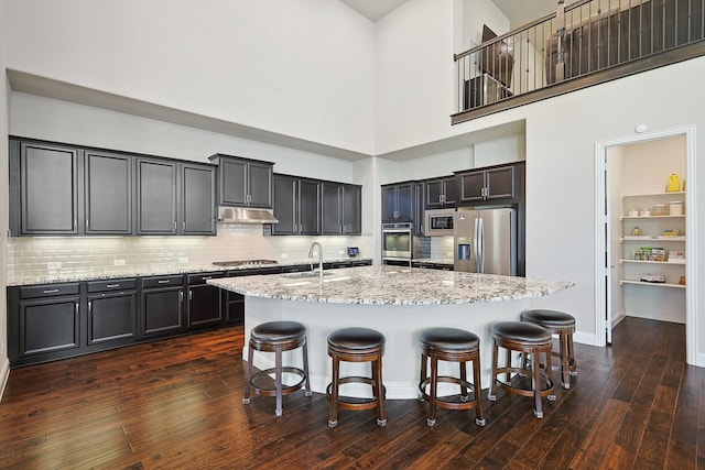 kitchen featuring an island with sink, stainless steel appliances, dark hardwood / wood-style flooring, a high ceiling, and a kitchen bar