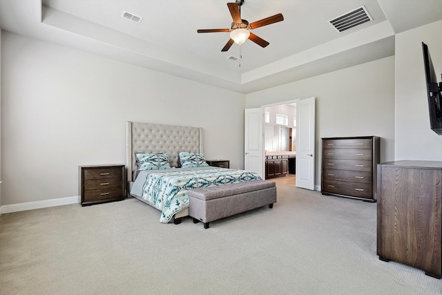 bedroom with ceiling fan, a raised ceiling, ensuite bath, and light carpet