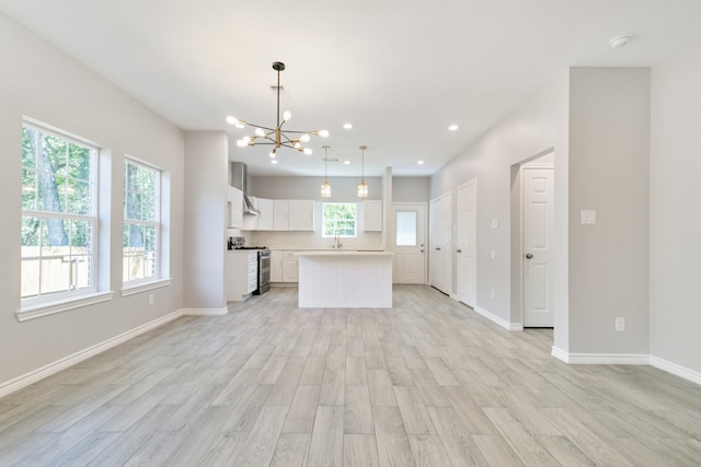 kitchen with white cabinets, hanging light fixtures, a kitchen island, stainless steel range with gas cooktop, and light hardwood / wood-style floors