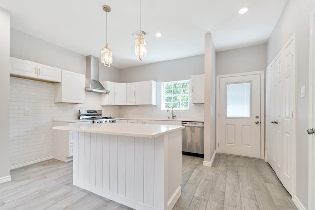 kitchen featuring appliances with stainless steel finishes, a kitchen island, wall chimney exhaust hood, and white cabinetry