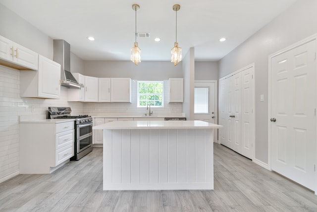 kitchen featuring white cabinets, range with two ovens, wall chimney exhaust hood, and light hardwood / wood-style flooring