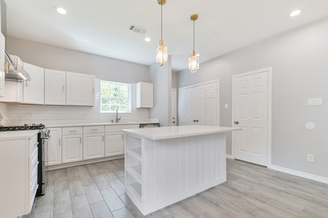 kitchen featuring a center island, white cabinets, stainless steel range with gas stovetop, light hardwood / wood-style flooring, and decorative light fixtures