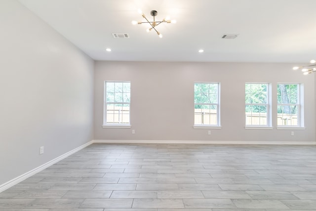 empty room featuring a chandelier, light wood-type flooring, and a healthy amount of sunlight