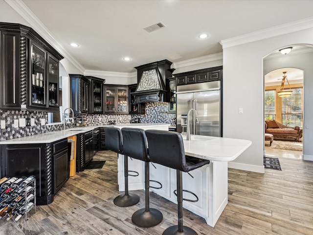 kitchen featuring decorative backsplash, custom range hood, light wood-type flooring, and stainless steel built in fridge