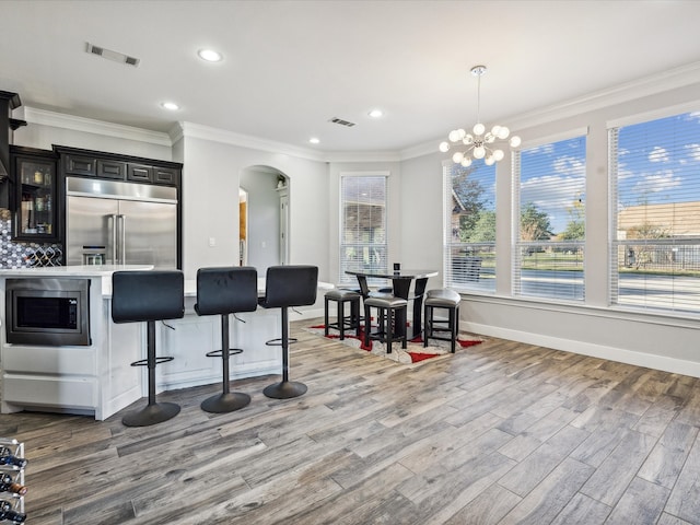 kitchen featuring a kitchen bar, ornamental molding, pendant lighting, built in appliances, and light hardwood / wood-style flooring