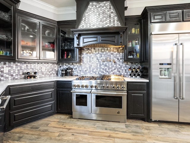 kitchen with high end appliances, crown molding, tasteful backsplash, and light hardwood / wood-style flooring