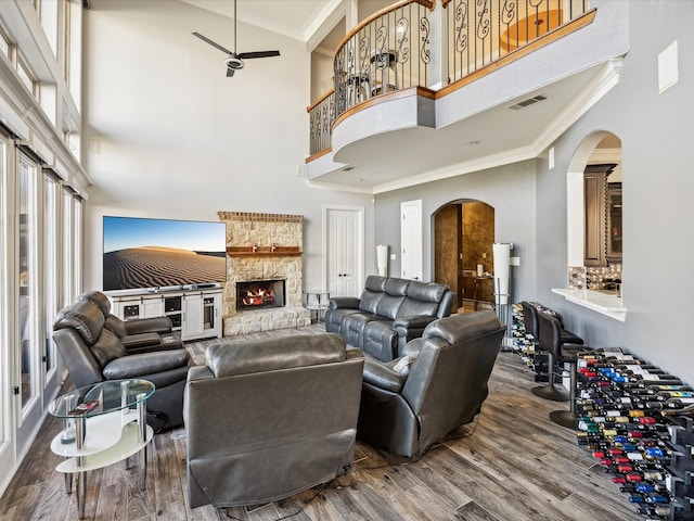 living room with a high ceiling, crown molding, hardwood / wood-style flooring, ceiling fan, and a fireplace