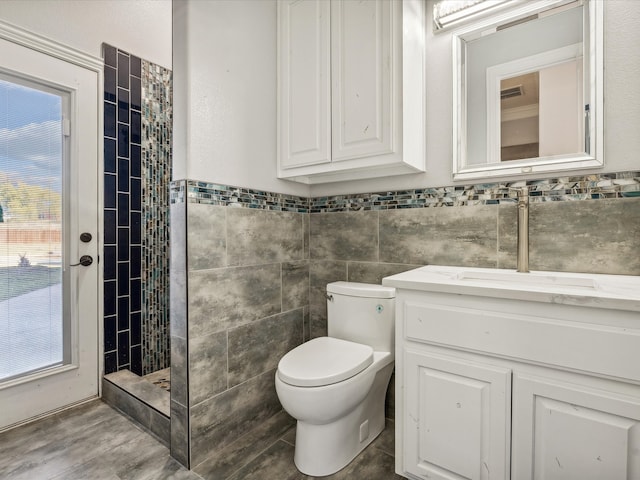 bathroom featuring vanity, toilet, tiled shower, and tile walls