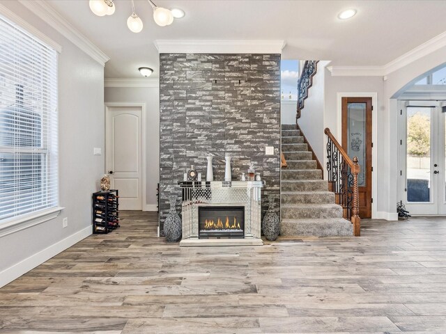 unfurnished living room featuring plenty of natural light, light wood-type flooring, crown molding, and a tiled fireplace