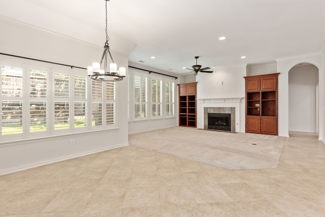 unfurnished living room with a tiled fireplace, ceiling fan with notable chandelier, and ornamental molding