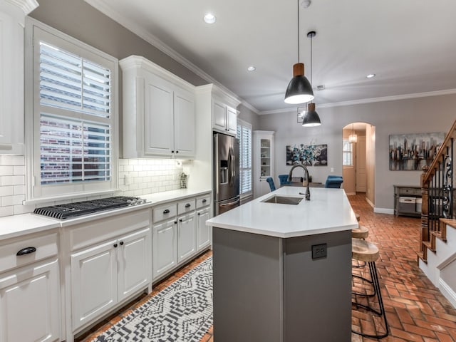 kitchen with an island with sink, sink, hanging light fixtures, white cabinetry, and appliances with stainless steel finishes