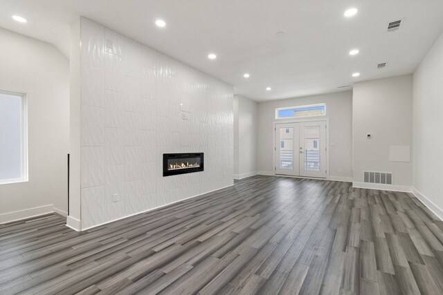 unfurnished living room with dark wood-type flooring, french doors, and a large fireplace