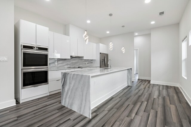 kitchen with pendant lighting, dark hardwood / wood-style flooring, a center island with sink, stainless steel appliances, and white cabinets