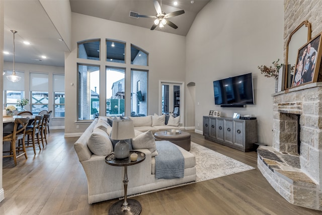 living room featuring light hardwood / wood-style floors, a stone fireplace, high vaulted ceiling, and ceiling fan