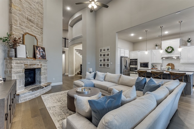 living room featuring a towering ceiling, dark hardwood / wood-style floors, a fireplace, and ceiling fan