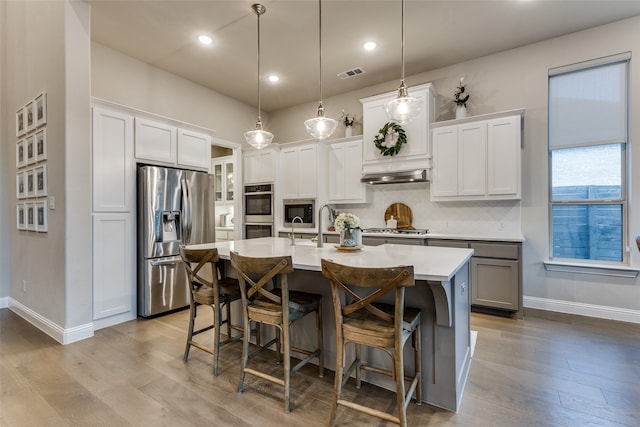 kitchen featuring a center island with sink, appliances with stainless steel finishes, pendant lighting, and white cabinets