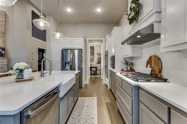 kitchen with extractor fan, pendant lighting, white cabinetry, appliances with stainless steel finishes, and light hardwood / wood-style floors