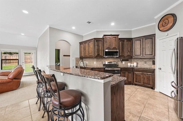 kitchen with dark brown cabinets, light tile patterned flooring, dark stone countertops, and appliances with stainless steel finishes