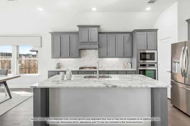 kitchen with sink, a center island with sink, light hardwood / wood-style flooring, appliances with stainless steel finishes, and light stone countertops