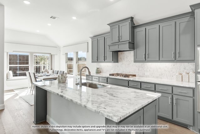 kitchen with a kitchen island with sink, gray cabinetry, light hardwood / wood-style flooring, vaulted ceiling, and sink