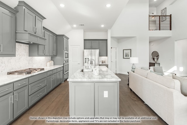 kitchen with appliances with stainless steel finishes, gray cabinets, dark hardwood / wood-style flooring, and an island with sink