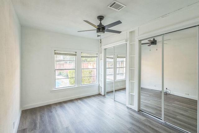 unfurnished bedroom with dark hardwood / wood-style flooring, two closets, and ceiling fan