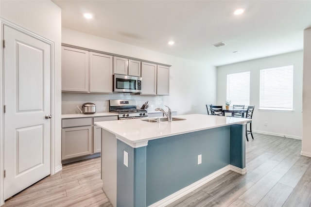 kitchen featuring light hardwood / wood-style flooring, an island with sink, stainless steel appliances, and gray cabinetry