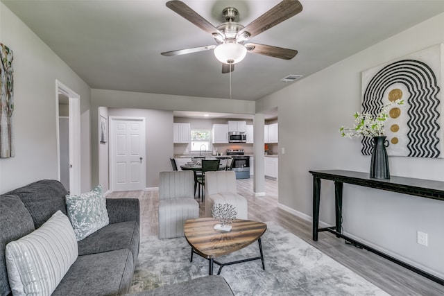 living room with sink, light wood-type flooring, and ceiling fan